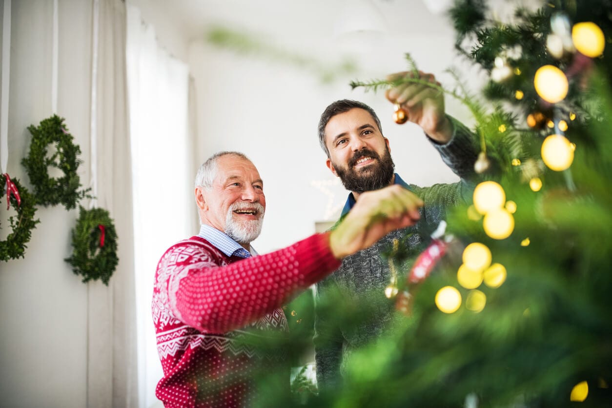 Ein junger Mann schmückt gemeinsam mit seinem demenzkranken Vater einen Weihnachtsbaum.
