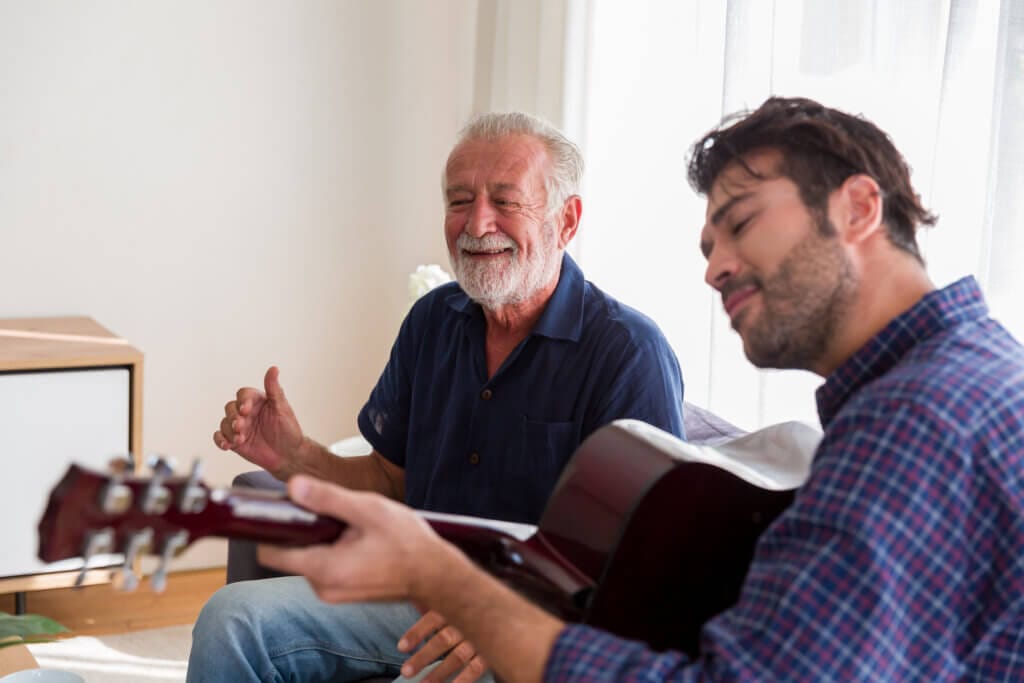 Ein junger Mann spielt Musik auf der Gitarre für seinen pflegebedürftigen Vater.