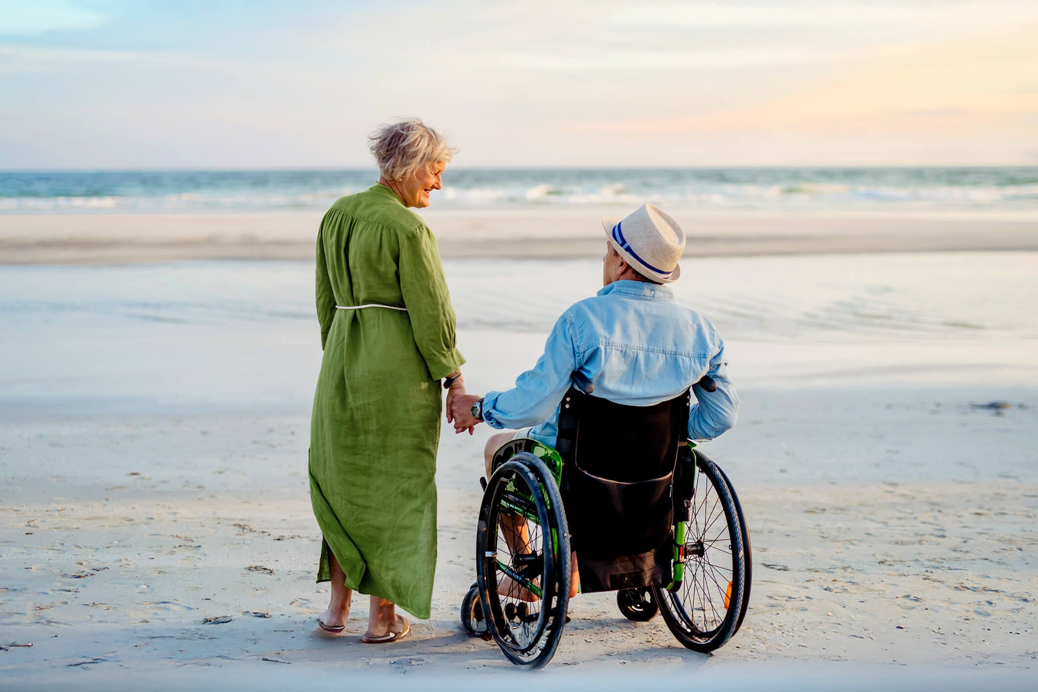 Eine pflegebedürftige Person im Rollstuhl und eine pflegende Angehörige am Meer.